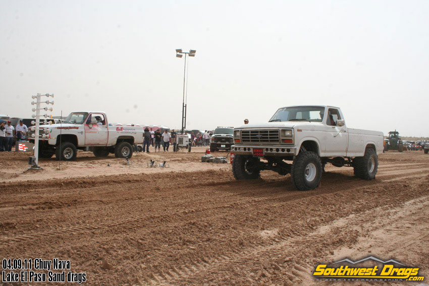 White lifted pickup truck with large tires on sand, front grille visible