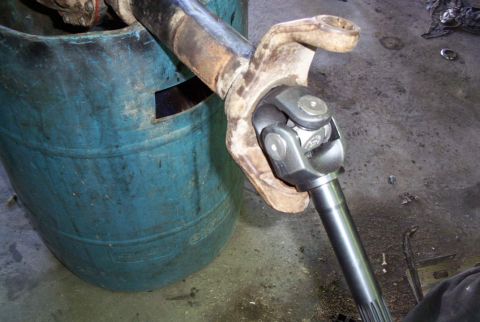1988 Ford Bronco - A driveshaft U-joint is held up, with a blue barrel in the background.