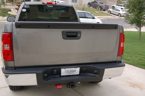 2007 Chevrolet Silverado 1500 - The rear of a gray pickup truck is shown, parked in a driveway with other vehicles visible in the background.