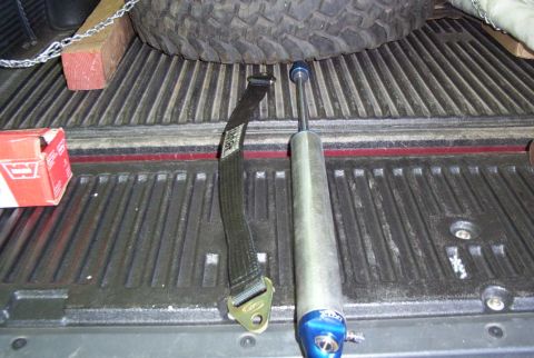 1988 Ford Bronco - A shock absorber and tie-down strap are visible in the bed of a truck, next to a spare tire.