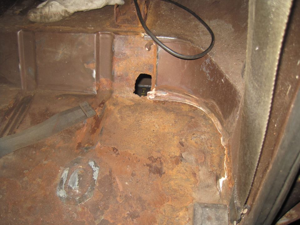 rusted interior floor pan with a hole and some wiring