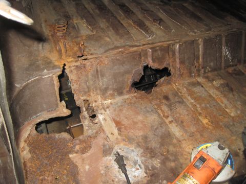 1979 Ford Bronco - The floor pan of a vehicle shows extensive rust damage and holes, with a grinding tool present.