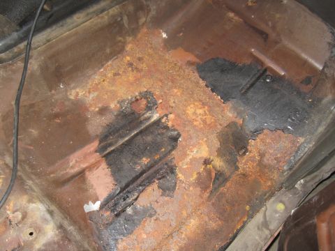 1979 Ford Bronco - The floor pan of a vehicle shows significant rust damage and areas of missing metal.