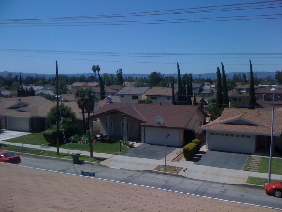 Suburban street with houses, trees, and a red car parked on the side