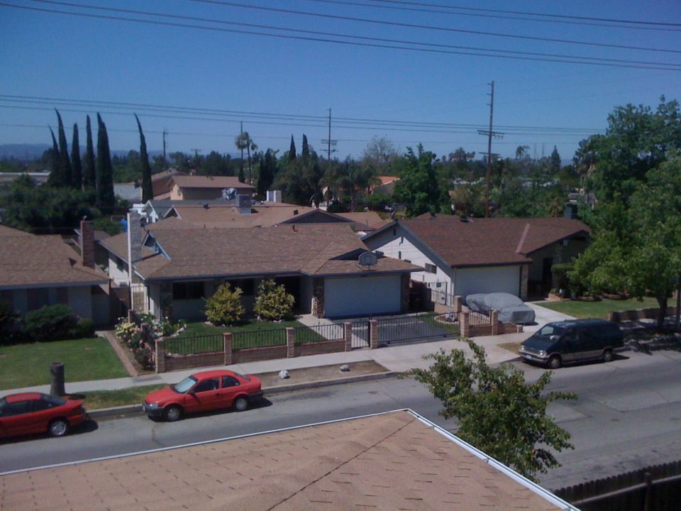 Street view with red cars parked, houses with brown roofs, and trees under a clear blue sky