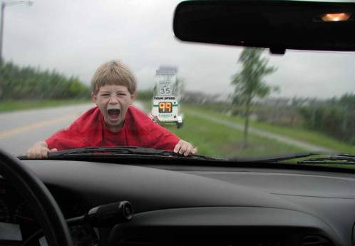 Windshield view from car dash of screaming child on hood past a 35 mph radar speed sign