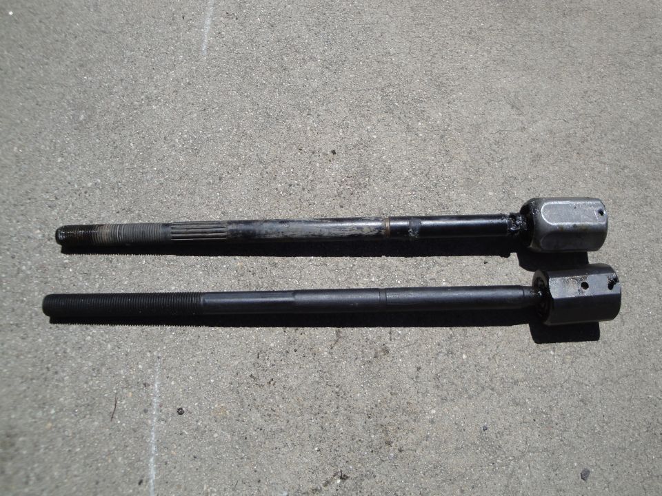 Two tie rod ends, one used and one new, laid on concrete