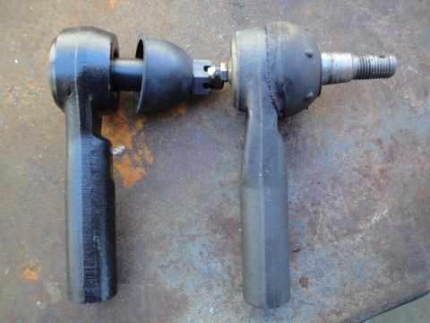 1995 Ford Taurus - Comparison of two tie rod ends, one black and one gray, against a textured, rusty background.