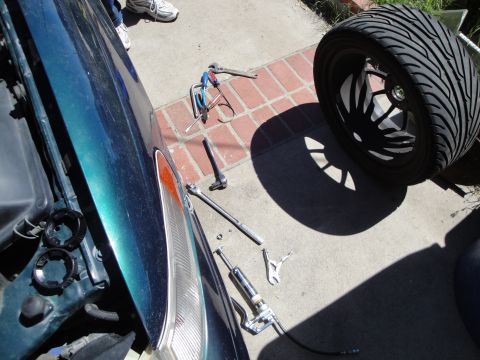 1995 Ford Taurus - Car repair in progress with tools and a spare wheel laid out on the ground next to the vehicle.
