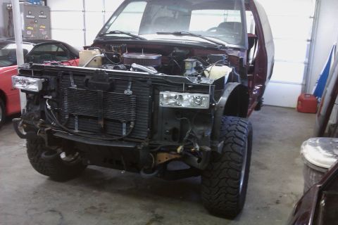 1994 Chevrolet Blazer - Front end of a maroon SUV, possibly a 1994 Chevrolet Blazer, is disassembled in a garage with the hood open and grille removed.