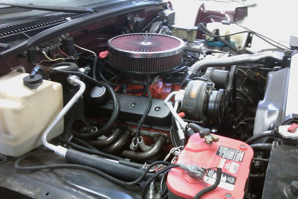 Engine bay showing V8 engine, air filter, battery, and hoses. Supermotors.net logo visible