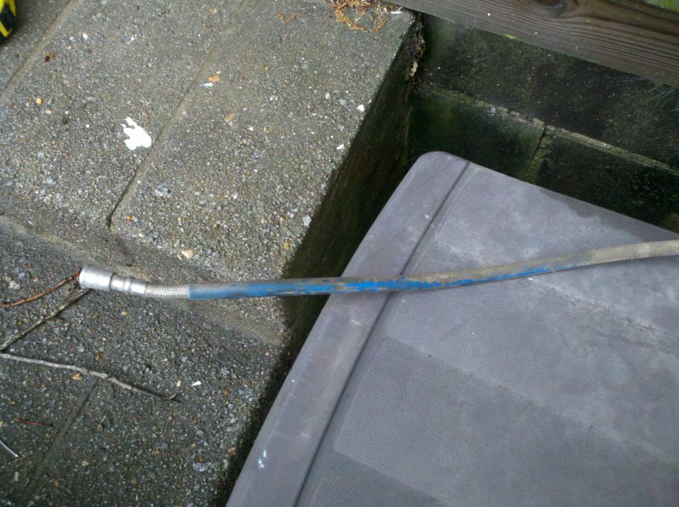 Blue-wrapped braided metal hose line resting on pavement and plastic
