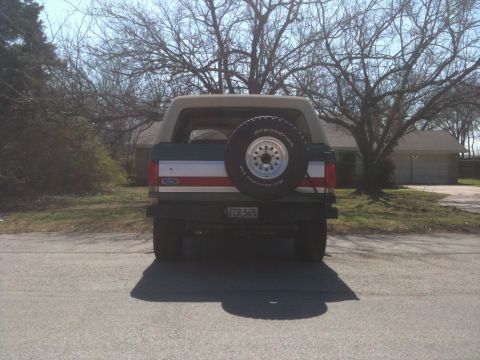 1989 Ford Bronco - This Ford Bronco is seen from the rear, a spare tire mounted on the tailgate and a distinctive red and white stripe on the rear panel.
