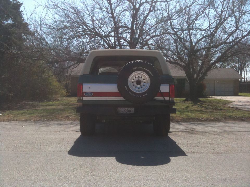 Rear view of a dark green Ford Bronco with a tan top and a spare tire on the tailgate