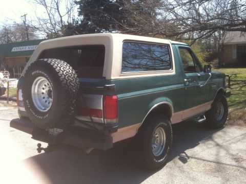 1989 Ford Bronco - This Ford Bronco is parked in front of an antique mall with trees and a house in the background.