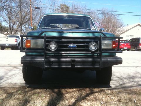 1989 Ford Bronco - Front view of a green Ford Bronco with a black brush guard and two round fog lights.