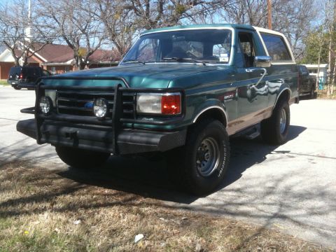 1989 Ford Bronco - A green 1987 Ford Bronco with a brush guard is parked on a street.