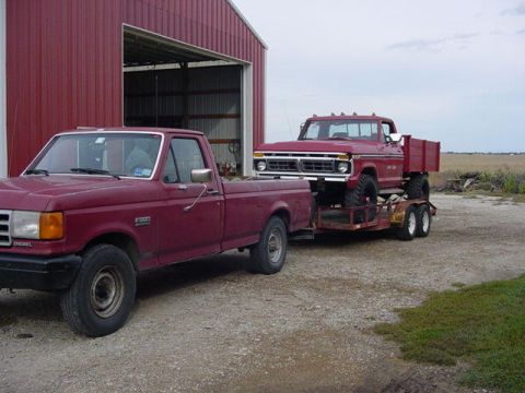 1992 Ford Bronco - A red 1970s Ford F-series truck is towed by another red Ford F-series truck in front of a barn.