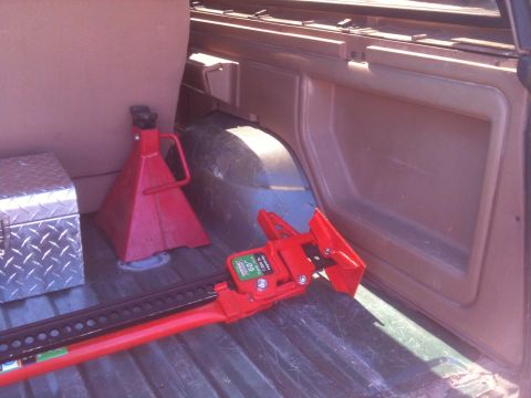 1989 Ford Bronco - The interior cargo area of a vehicle contains a red hi-lift jack, a red jack stand, and a diamond plate toolbox.