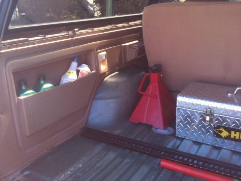 1989 Ford Bronco - Vehicle interior cargo area contains cleaning supplies, a jack, and a toolbox.