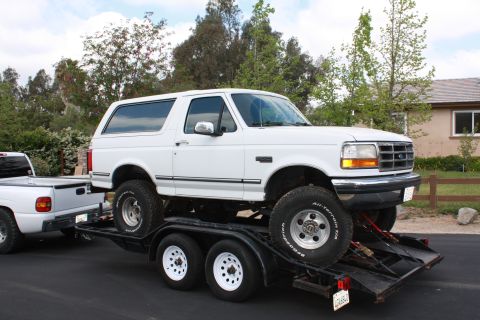 1992 Ford Bronco - A white 1992 Ford Bronco is loaded onto a trailer, showing its lifted stance and off-road tires.