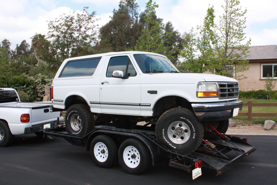 White 1992 Ford Bronco on a trailer, front 3/4 view, lifted, with off-road tires