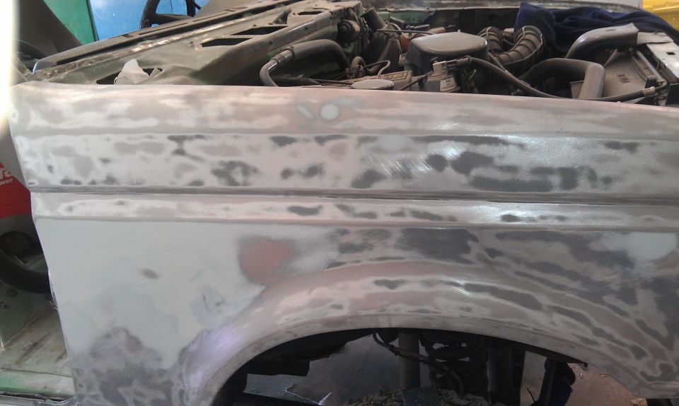 Car fender with primer and body filler, showing engine components in the background