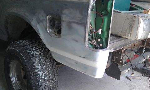 1995 Ford Bronco - The rear quarter panel of a Ford Bronco shows bodywork in progress, with the fuel filler door and tire visible.