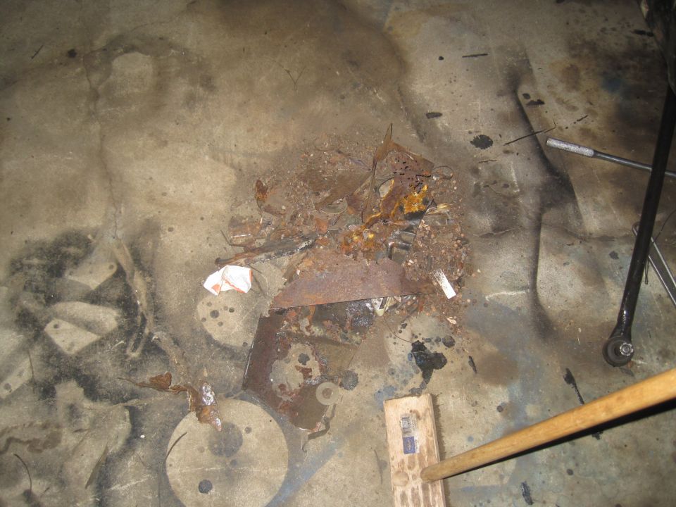 pile of rusty metal parts and debris on concrete floor with a broom handle nearby