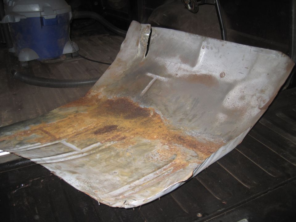 Rusted metal floor pan with a T-shaped indentation, seen from above