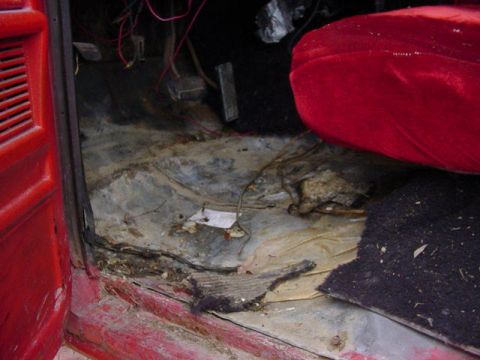 1992 Ford Bronco - The interior of a red vehicle shows a damaged floor and exposed wiring, with a red seat visible.