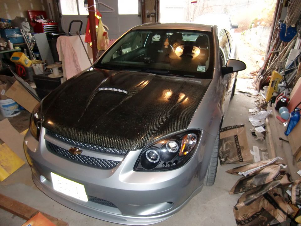 Silver Chevrolet Cobalt coupe with carbon-fiber hood in cluttered garage
