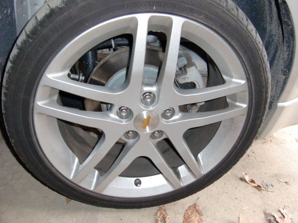 Silver Chevrolet five-spoke alloy wheel with bowtie cap showing disc brake and caliper