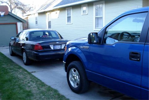 2008 Ford Crown Victoria - A dark blue sedan is parked in a driveway next to a blue pickup truck.