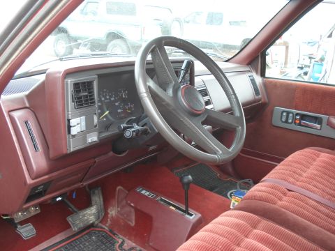1994 GMC Sierra 3500 - The interior of a 1994 GMC Sierra 3500 features a red velour bench seat and a dashboard with a prominent steering wheel and instrument clus…