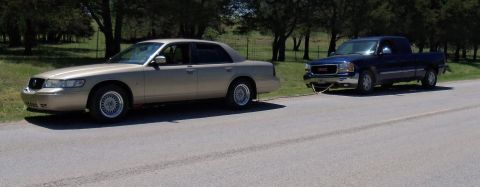 2000 Mercury Grand Marquis - A 2000 Mercury Grand Marquis is being towed by a GMC Sierra pickup truck on a paved road.