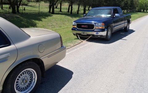 2000 Mercury Grand Marquis - A GMC pickup truck is towing a sedan down a road, connected by a chain.
