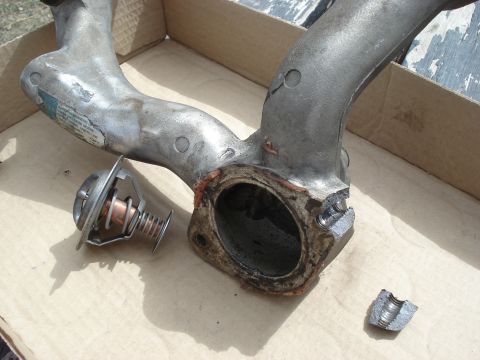 1994 GMC Sierra 3500 - A removed thermostat and its housing sit on a cardboard surface, showing signs of wear and tear.
