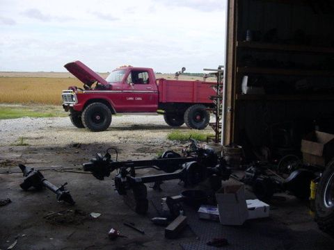 1992 Ford Bronco - A red pickup truck, possibly a 1977 Ford F-250, sits outside a garage with its hood open and "Lawn Care" written on the door.