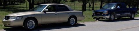 2000 Mercury Grand Marquis - A 2000 Mercury Grand Marquis is parked on the side of the road next to a GMC pickup truck.