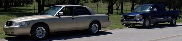 Gold 2000 Mercury Grand Marquis parked next to a blue GMC pickup truck