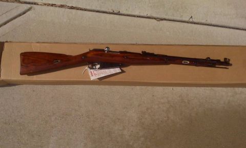 2003 Ford Crown Victoria - A rifle with a wooden stock rests on a cardboard box, with some papers underneath.