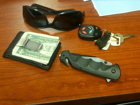 1987 Ford Bronco - A collection of personal items including sunglasses, a wallet, keys, and a knife are laid out on a wooden desk.