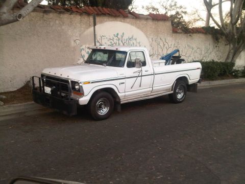 1986 Ford Bronco - This white Ford pickup truck, likely from the late 1970s, is parked in front of a stucco wall with a mural.