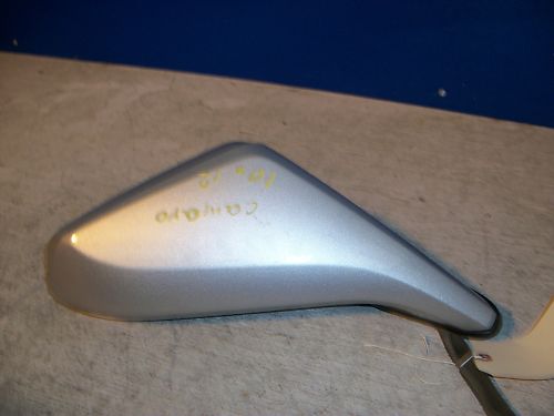 Silver exterior side mirror part with yellow handwritten marking, laid on white surface