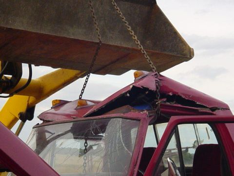 1992 Ford Bronco - A red pickup truck cab with a severely damaged roof is being lifted by chains attached to an excavator.