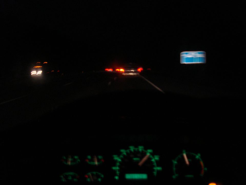 Dashboard gauges glow green at night, with blurry headlights and taillights of other vehicles visible on a highway