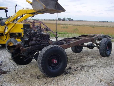1992 Ford Bronco - A truck chassis with its engine is being lifted by a yellow loader in a field.