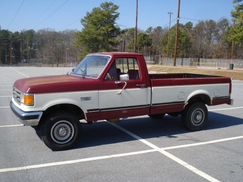 1989 Ford F-250 - A two-tone red and white Ford F-Series pickup truck is parked in an empty lot on a sunny day.