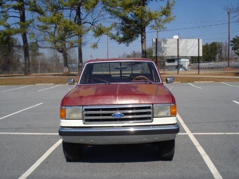 1989 Ford F-250 - A red and white Ford F-250 truck is parked head-on in a parking lot under a clear sky.